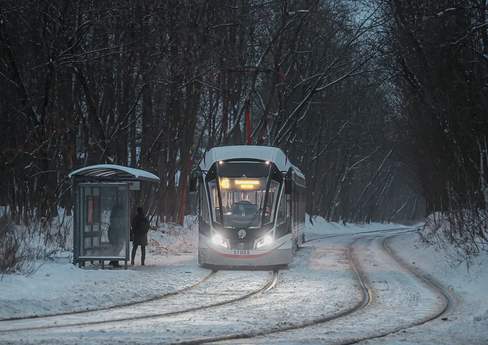 A tram arrives at a snowy forest stop in winter, highlighting solitude and travel.