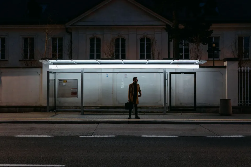 Man standing alone at a bus stop during night, with street lights illuminating the scene.