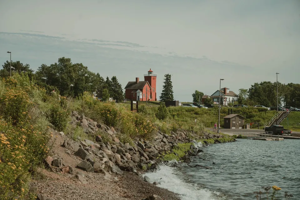 Idyllic lighthouse on Lake Superior's rocky shore in Duluth, Minnesota, surrounded by lush greenery.