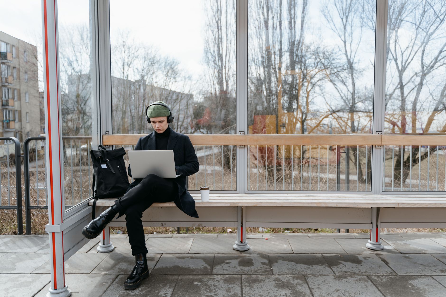 A young man works remotely on a laptop while sitting at a bus stop, showcasing modern digital nomad life.
